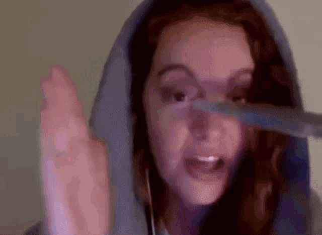 a woman in a blue hoodie is holding a pair of scissors in her hand .