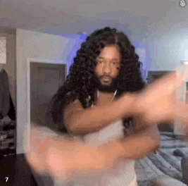 a man with long curly hair and a beard is standing in a room .