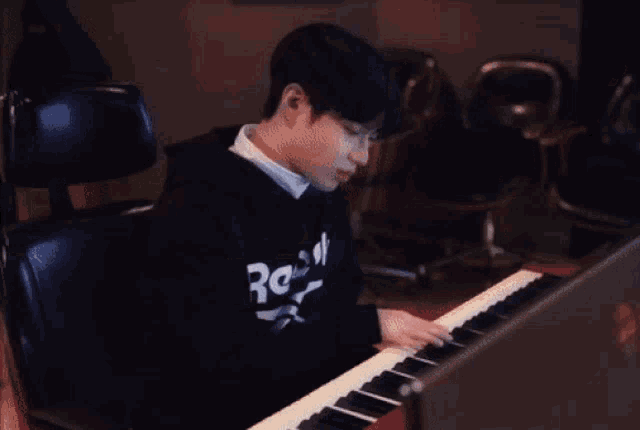 a person wearing a black reebok shirt is playing a piano