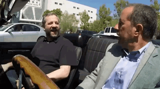 two men are sitting in a car with a sign that says parking here
