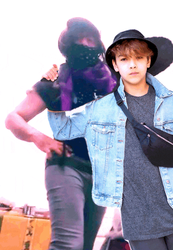 a boy wearing a denim jacket and a black hat stands next to a man wearing a mask