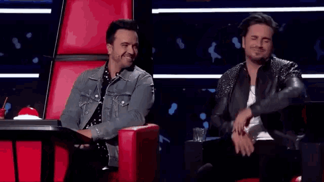 two men are sitting in red chairs with their arms in the air and laughing .