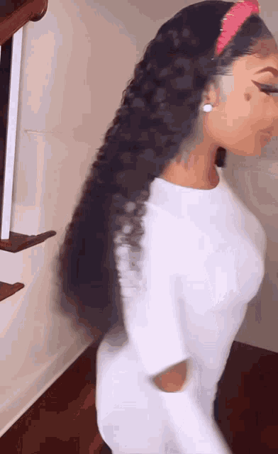 a woman with long curly hair wearing a white dress and a pink headband