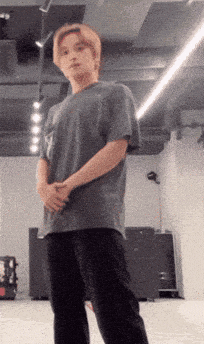 a man in a gray shirt and black pants is standing in a room with his hands folded