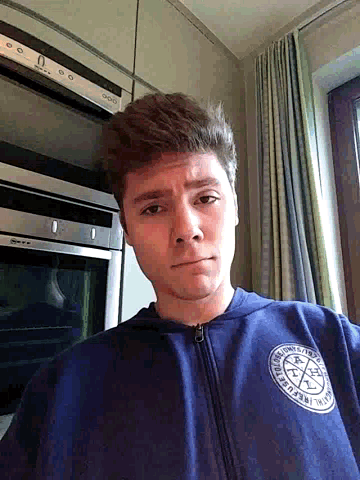 a man wearing a blue sweatshirt that says ' r.l.c. ' on it stands in front of an oven