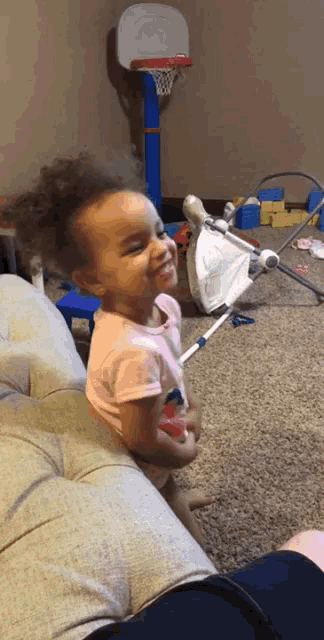 a little girl is smiling while sitting on a couch in front of a basketball hoop