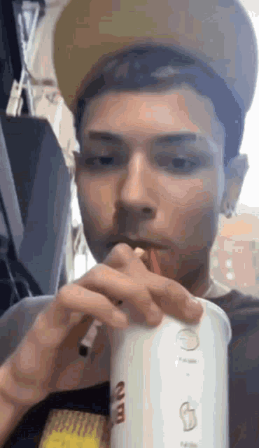a man wearing a hat is drinking from a cup with a straw .