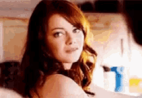 a woman with red hair is looking over her shoulder at the camera while standing in a kitchen .