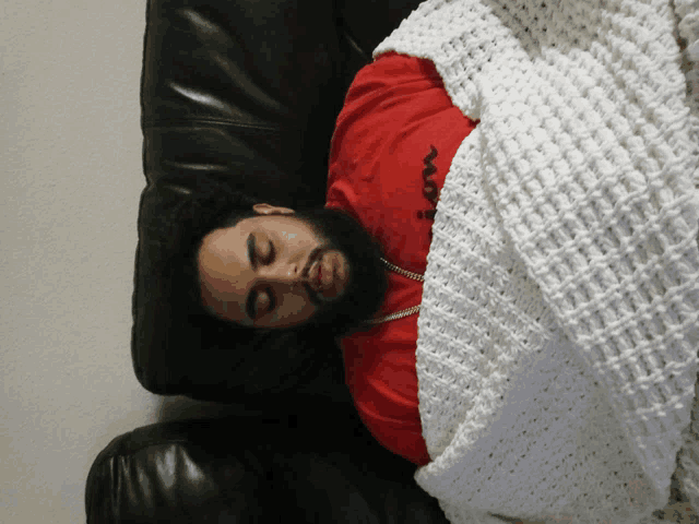 a man in a red shirt is sleeping on a couch with a white blanket over him