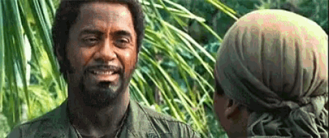 a man in a military uniform is smiling while talking to another man in a jungle .