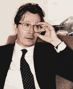 a man in a suit and tie is adjusting his glasses while sitting in a chair