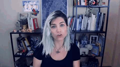 a woman with blue hair is standing in front of a bookshelf filled with books