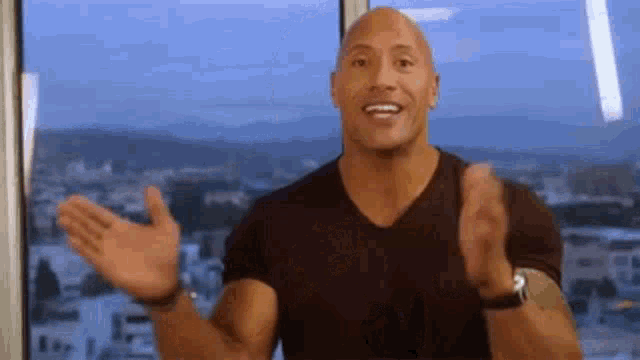 a bald man is standing in front of a window with his hands outstretched and smiling .