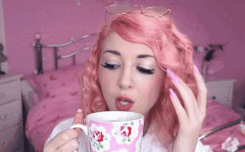 a woman with pink hair is drinking a cup of tea in a pink room .