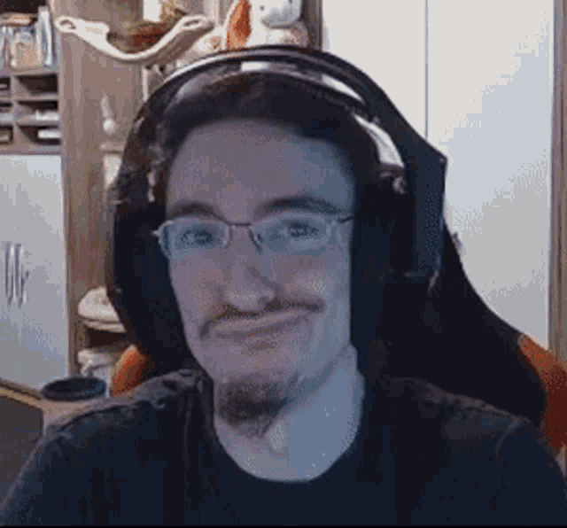 a man wearing headphones and glasses is smiling in front of a computer screen .