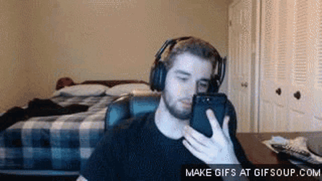 a man wearing headphones is using a cell phone in a bedroom .