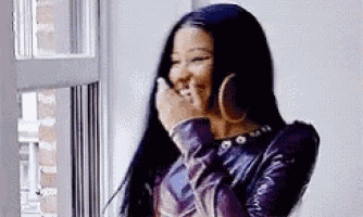 a woman is laughing and covering her mouth with her hand while standing next to a window .