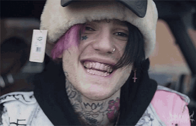a young man with pink hair and a tattoo on his face is smiling