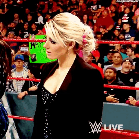 a woman stands in a wrestling ring holding a sign that says " may "
