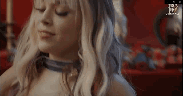 a woman with blonde hair and a choker looks at the camera with a screen saver that says ' scream ' on it