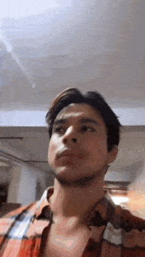 a man in a plaid shirt is standing in a room and looking up at the sky .