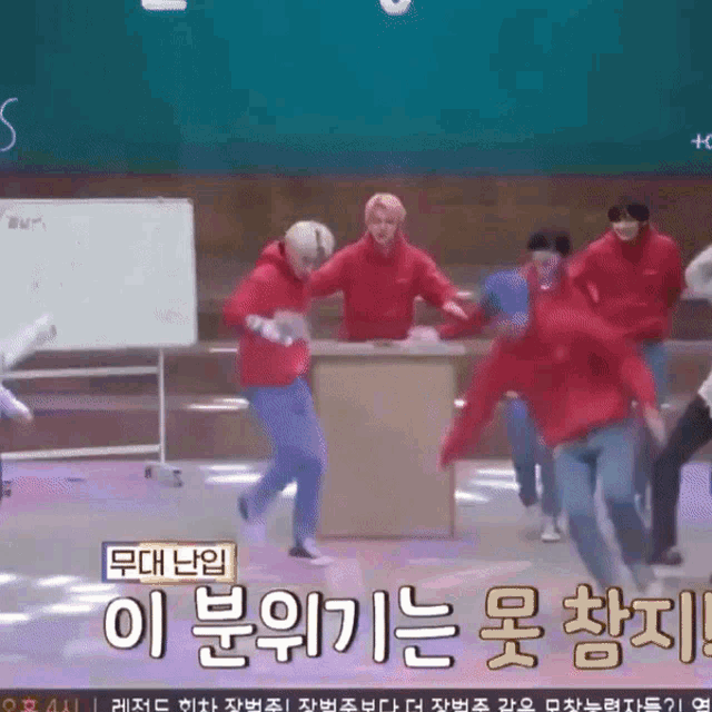 a group of people in red sweatshirts are dancing in front of a whiteboard with korean writing on it
