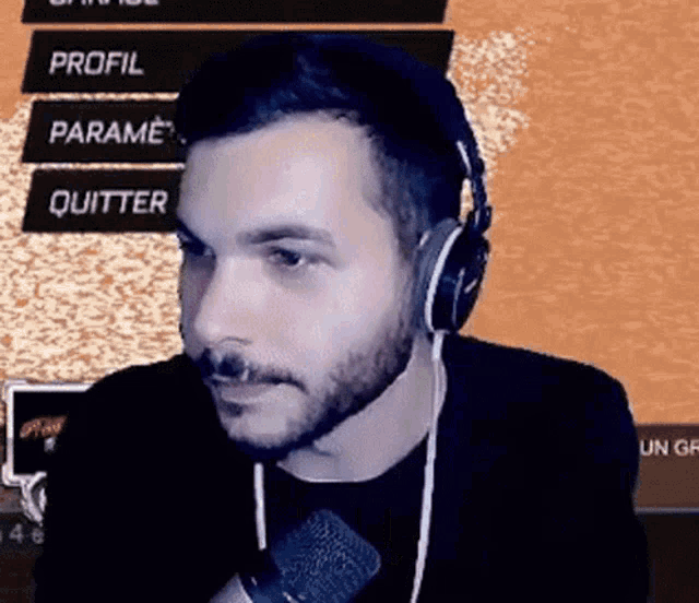 a man with a beard wearing headphones and a microphone in front of a screen that says profil