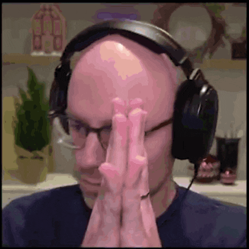 a bald man wearing headphones is praying with his hands on his face