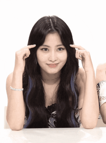 a woman with long black hair is making a heart with her fingers