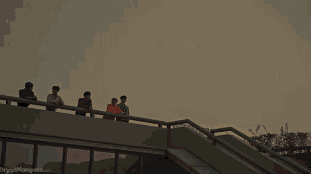 a group of young men are sitting on a balcony and the website dryedmangoez.com is displayed in the corner