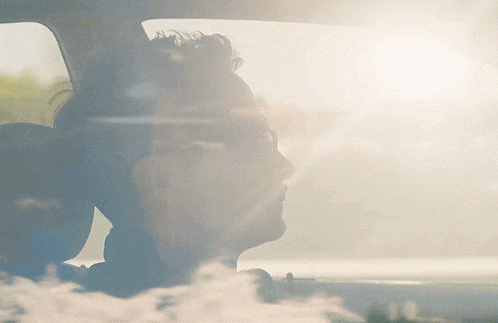 a man sitting in a car with the sun shining through the windshield