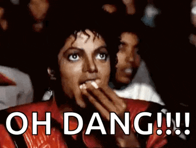 a man in a red jacket is eating popcorn while watching a movie and says `` oh dang !!! '' .