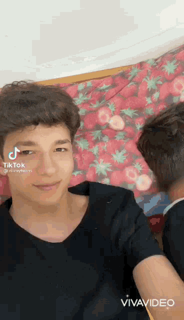 a young man is sitting on a bed with a strawberry blanket on it .