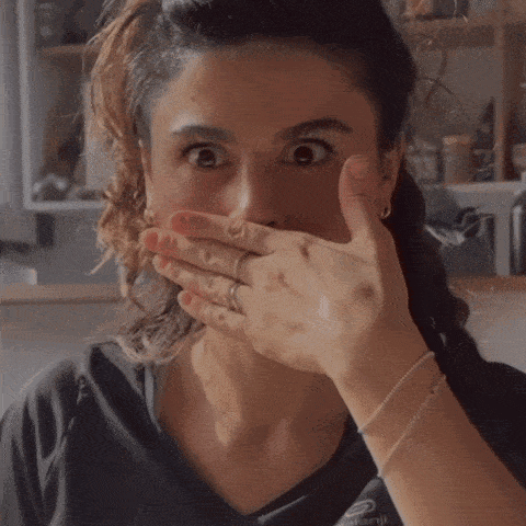 a woman covering her mouth with her hand while looking at the camera