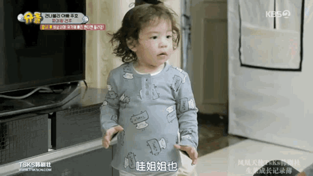 a little girl is standing in front of a television with chinese writing on the screen