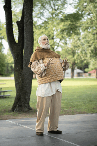 a man with a beard is standing on a stage in front of trees