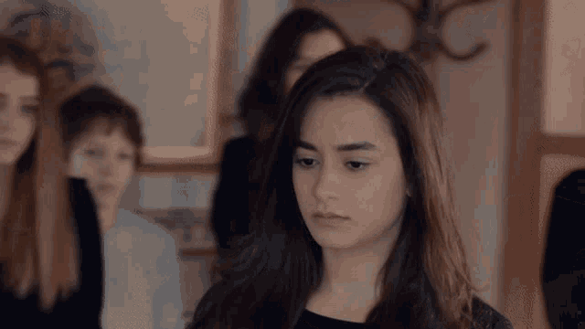 a girl in a black dress stands in a room with other people