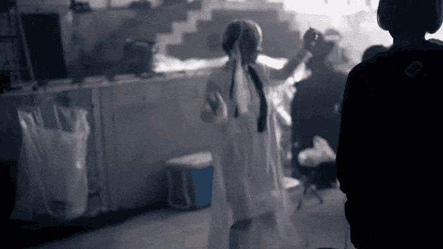 a woman in a white dress stands in a dark room