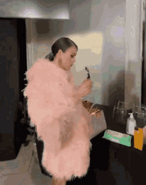 a woman in a pink fur coat is standing in front of a mirror