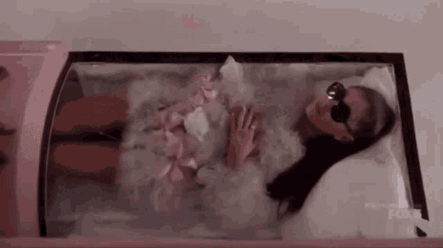a woman is laying in a pink coffin wearing sunglasses