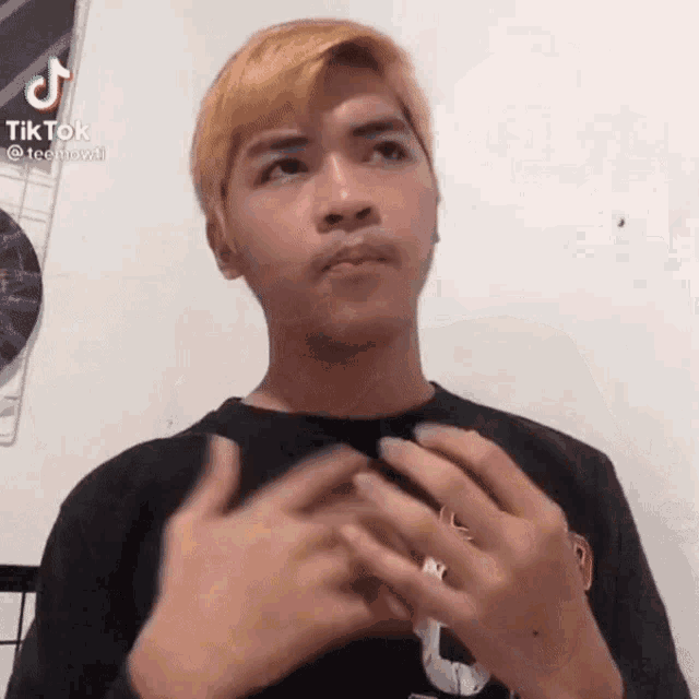 a young man with blonde hair is making a funny face while holding his hands together .