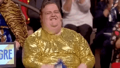 a fat man is wearing a gold sequined shirt and smiling while sitting in a crowd of people .