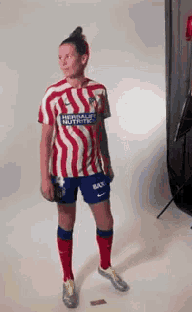 a woman in a red and white striped soccer jersey is standing in front of a white wall .