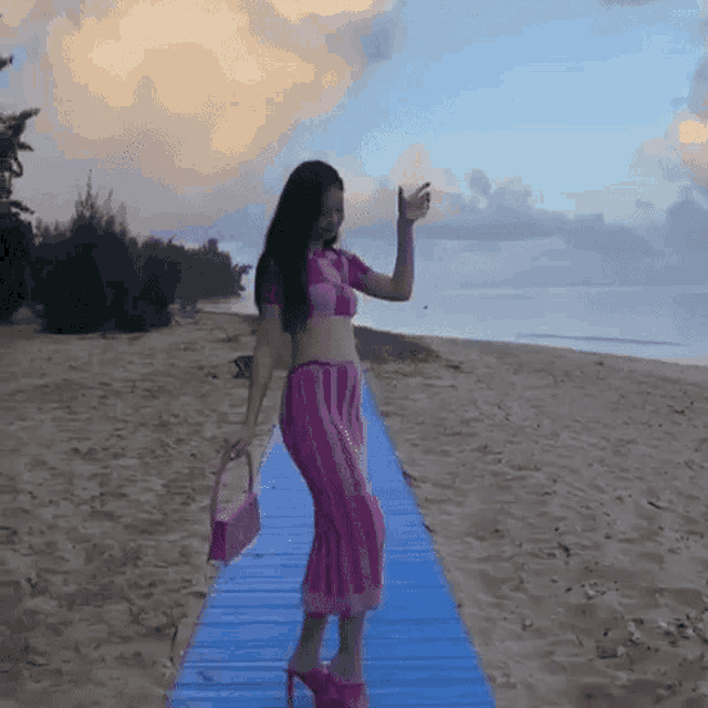 a woman in a pink dress and pink heels is standing on a blue walkway on the beach .