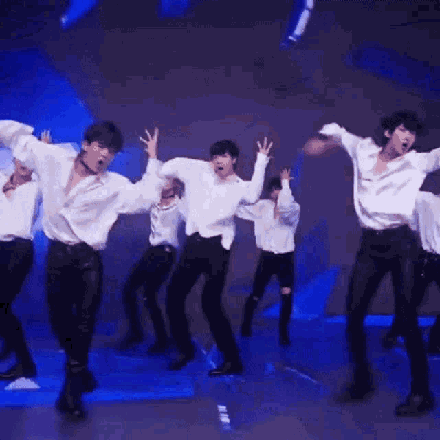 a group of men in white shirts and black pants are dancing on a stage .