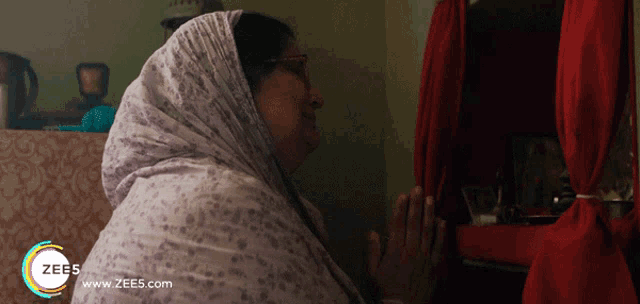 a woman is praying in front of a red curtain with the website www.zees.com visible