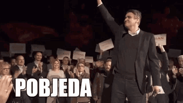 a man in a suit is standing in front of a crowd with the word pobjeda on the bottom right