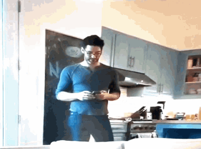 a man in a blue shirt is standing in a kitchen looking at his cell phone