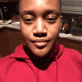 a woman in a red hoodie is making a funny face in a kitchen
