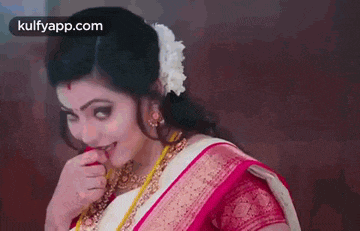 a woman in a pink and white saree is biting her finger .